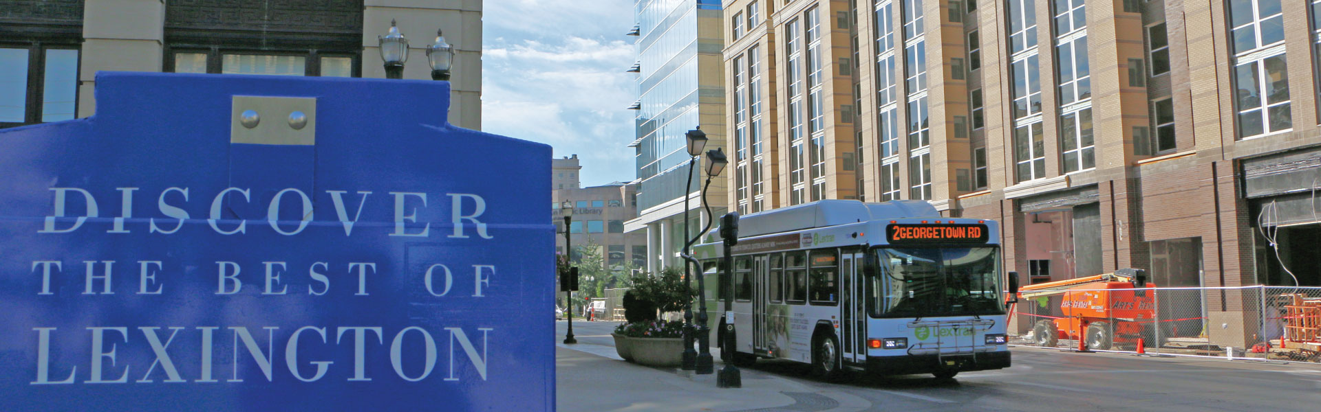 A sign that says "discovery the best of lexington" and a bus in the background.